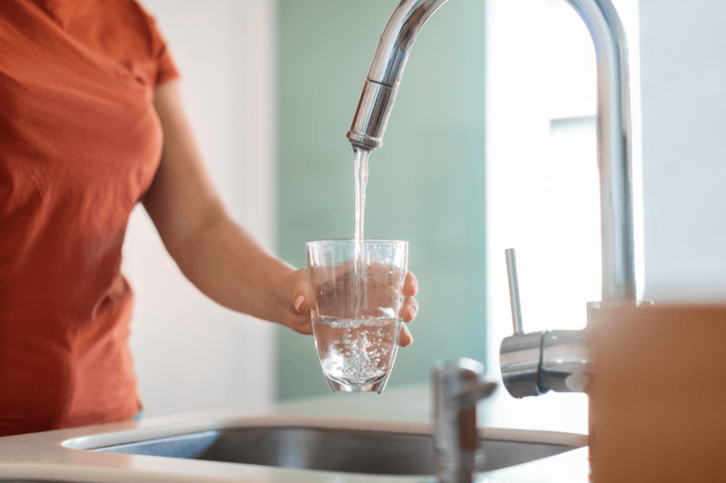 Rent og blødt drikkevand hældes i glas fra vandhane – resultatet af effektivt blødgøringsanlæg og korrekt brug af blødgøringssalt, der fjerner kalk og forbedrer vandkvaliteten.